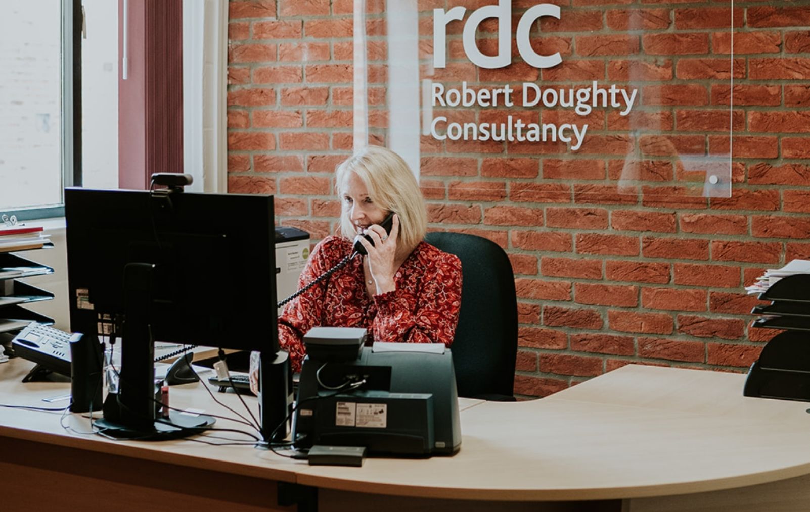 A woman sat behind a reception desk on the phone
